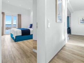 Ein Schlafzimmer mit Bett, Blick durch eine Glastür und einem Gang zu einem weiteren Raum.