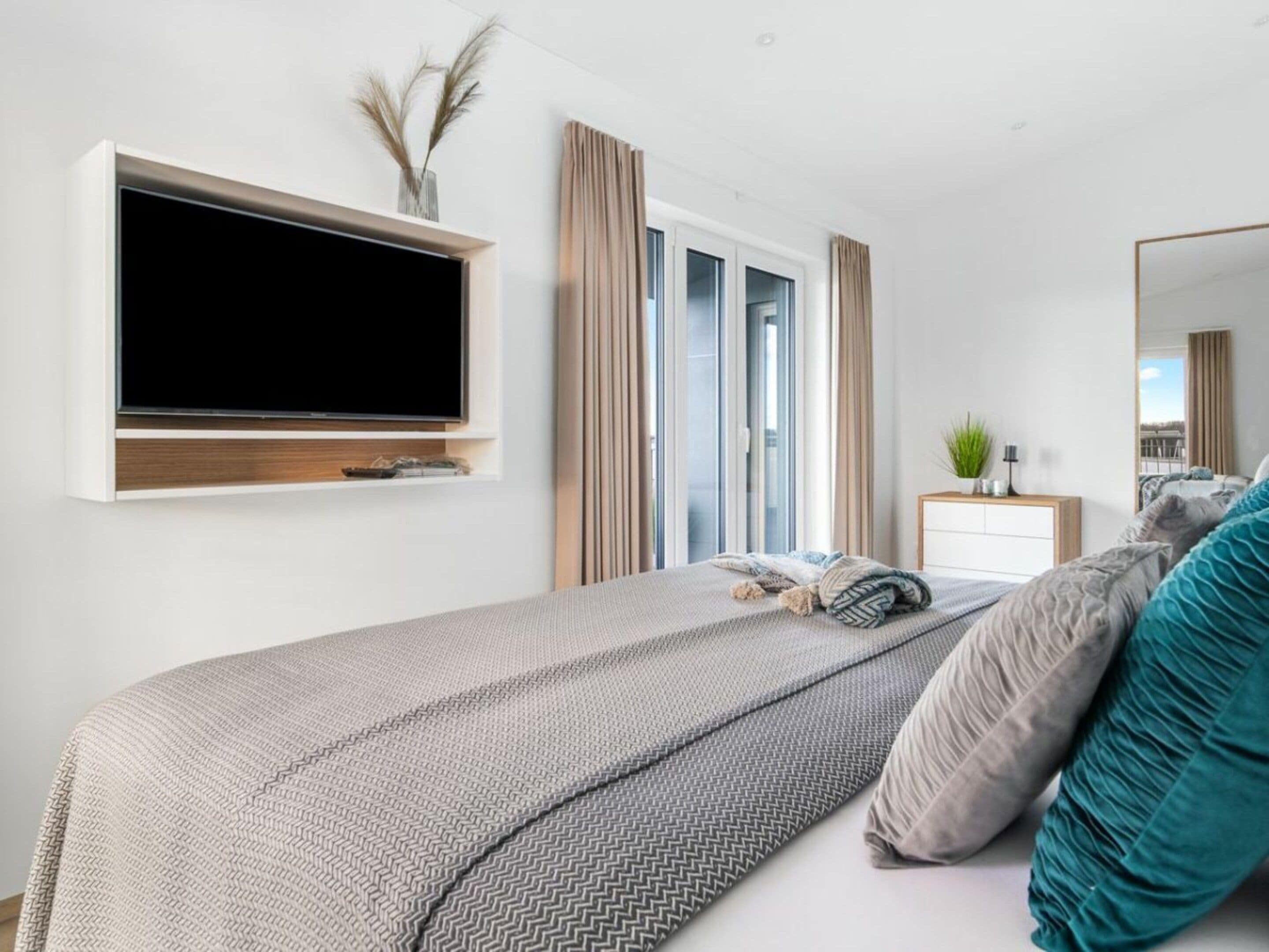 A modern bedroom with a bed, a TV mounted on the wall, a bedside table, and a window with curtains.