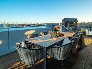 A rooftop terrace with a table set for dining, wicker chairs, and a view of the water and cityscape. - Holiday Apartment With 4 Bedrooms (Kappeln)