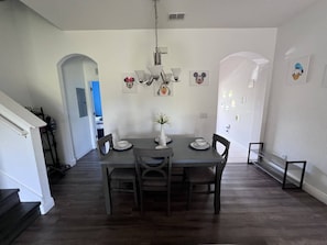 A dining area with a table set for four, chairs, a vase with flowers, and wall decorations including cartoon characters. - Regal Palms 3BR Gated TH sleeps 10 guests- Bergamo (Davenport)