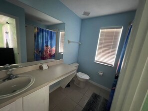 Baño con lavamanos, inodoro y ventana con persianas.