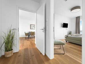 A modern interior with a wooden floor, a dining area with chairs, a bed with a green cushion, and a flat-screen TV mounted on the wall. - Apartment in Olpenitz With Swimming Pool (Kappeln)