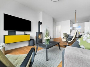 Un salon moderne avec un téléviseur à écran plat, un poêle à bois noir, un meuble de rangement jaune et gris, un canapé gris et un fauteuil vert.