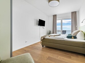 Une chambre à coucher avec un lit, un téléviseur fixé au mur, une fenêtre avec des rideaux et un balcon.