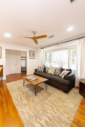 A modern living room with a dark grey sofa, a wooden coffee table, and a ceiling fan. - Charming 4-bedroom split-level home in North Charleston (North Charleston)