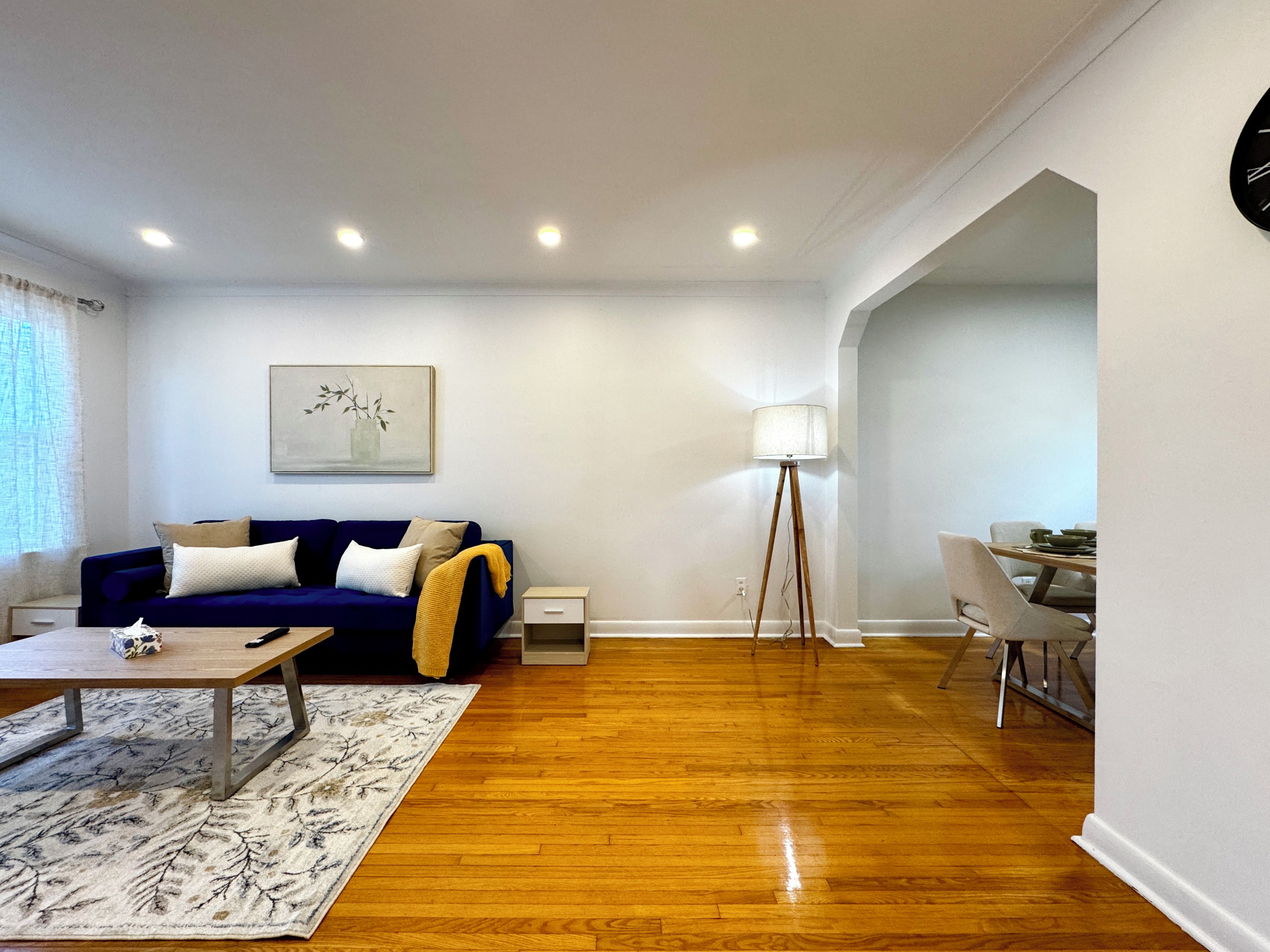 A modern living room with a blue sofa, a coffee table, a floor lamp, and a dining area with a table and chairs.