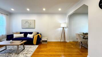 A modern living room with a blue sofa, a coffee table, a floor lamp, and a dining area with a table and chairs.