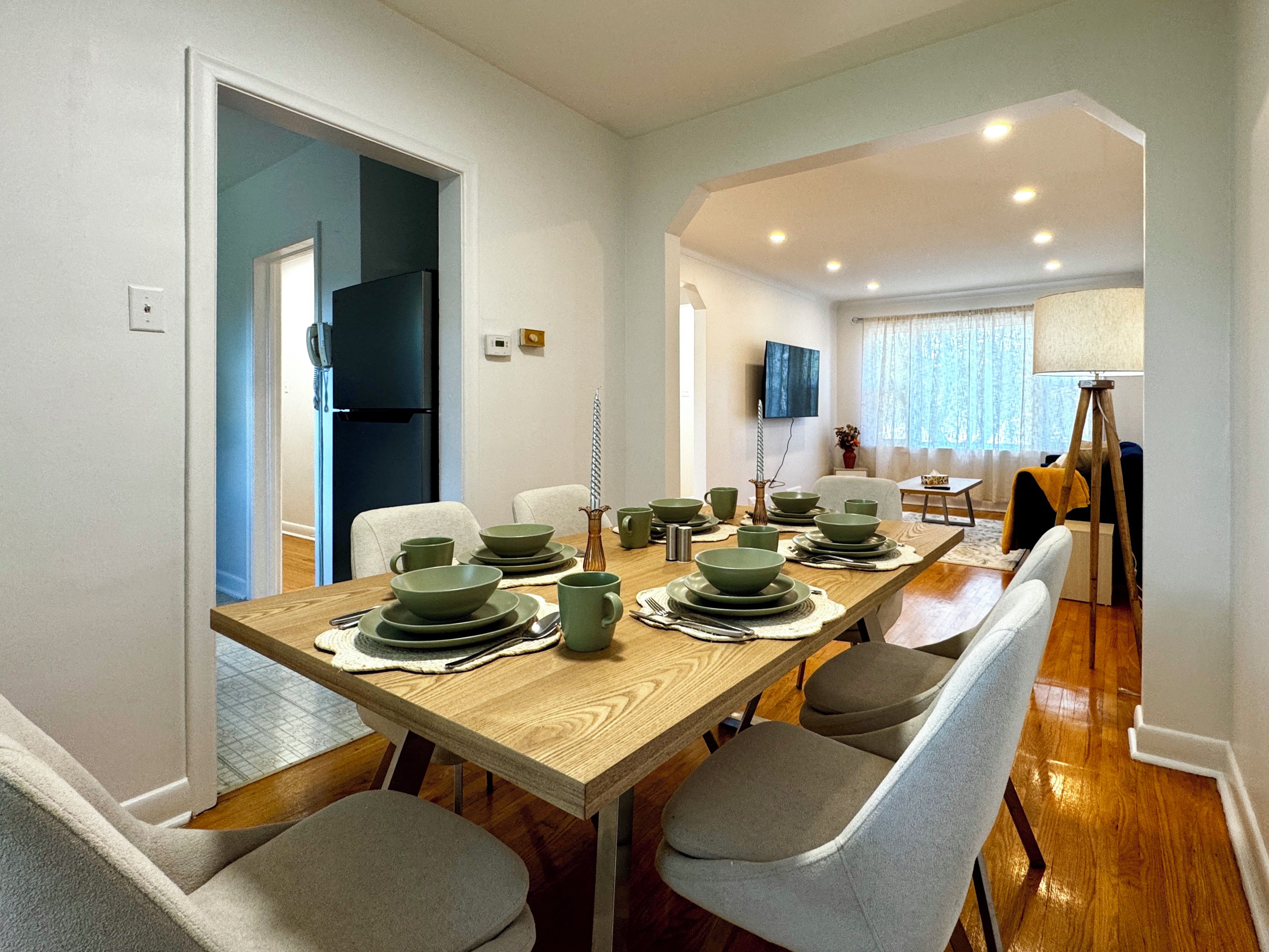 A dining area with a long wooden table set for four, surrounded by grey chairs.