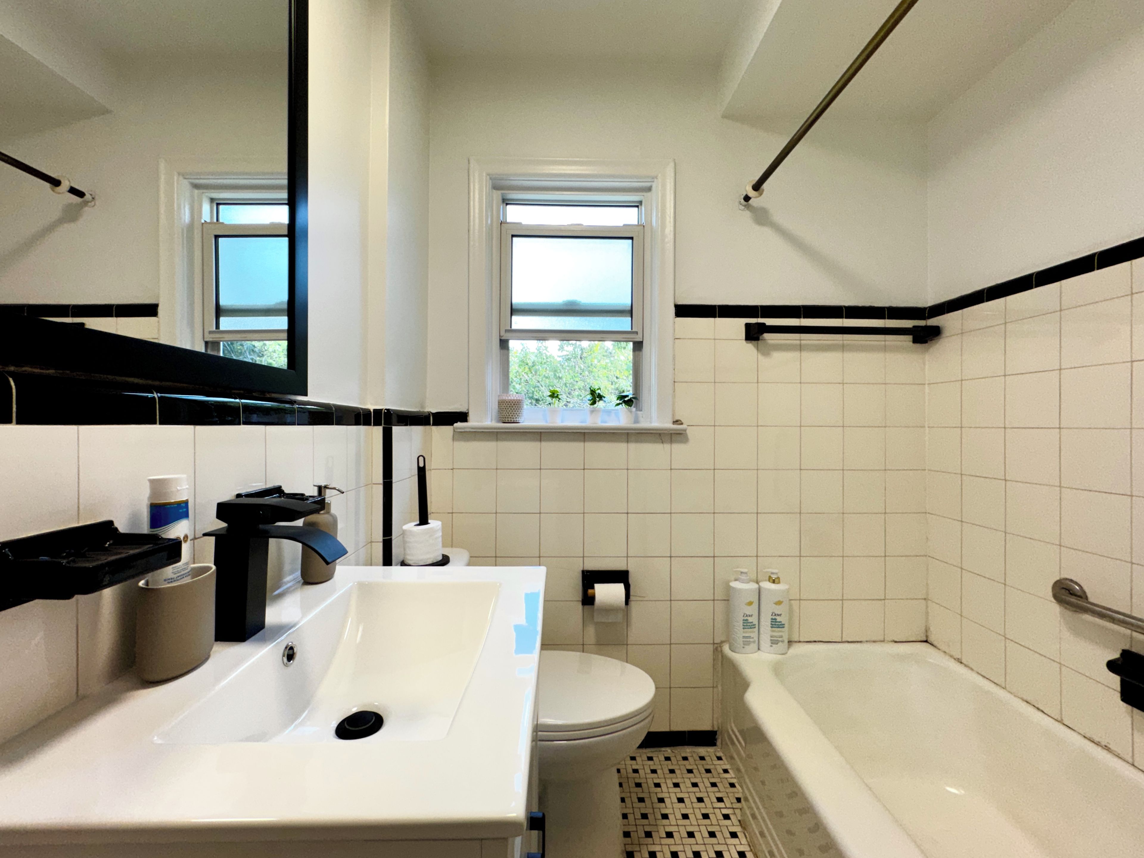 A bathroom with a sink, toilet, and bathtub. There is a window above the toilet and a towel rack above the bathtub.