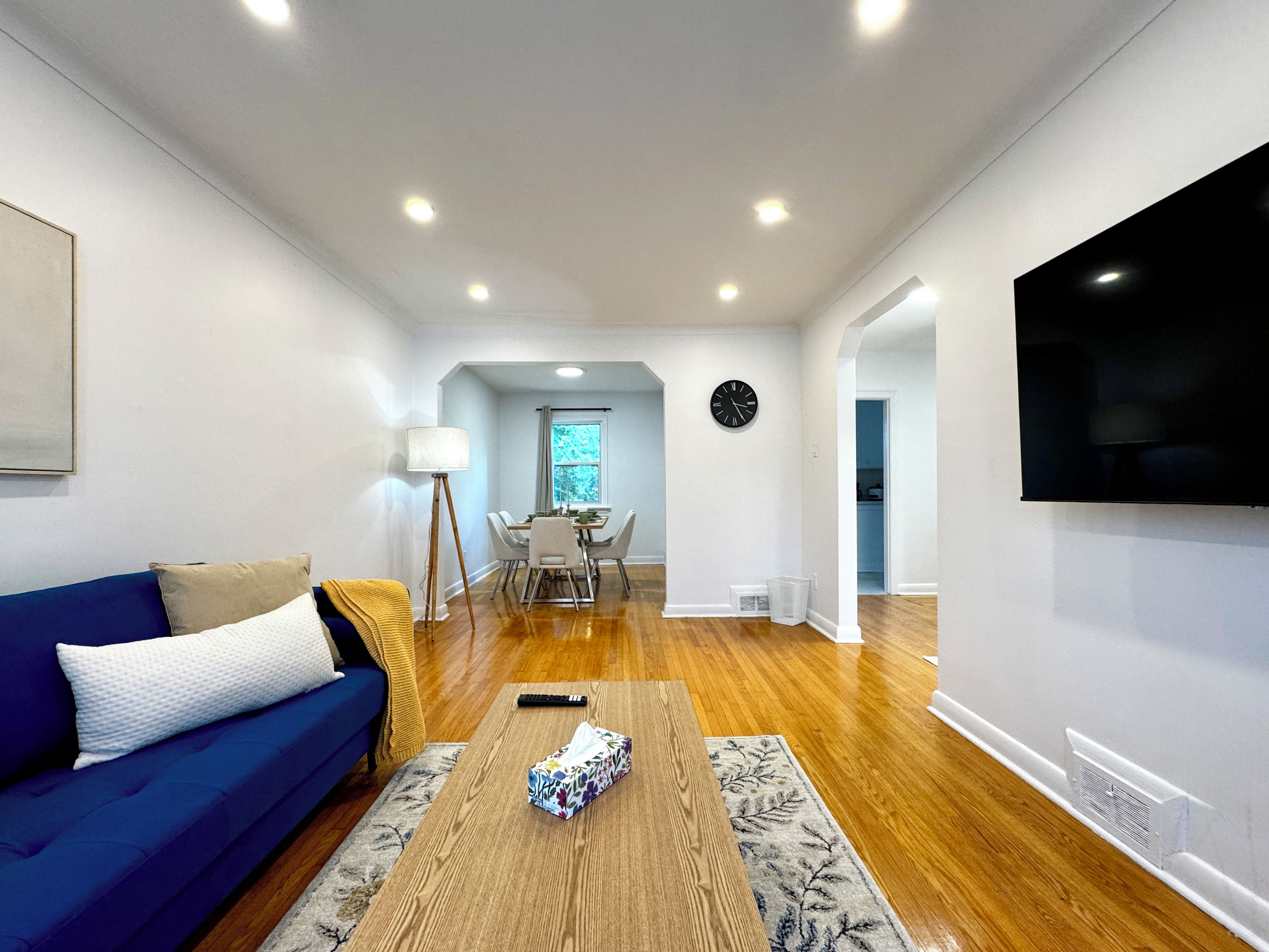 A modern living room with a blue sofa, a wooden coffee table, and a dining area with a table and chairs.
