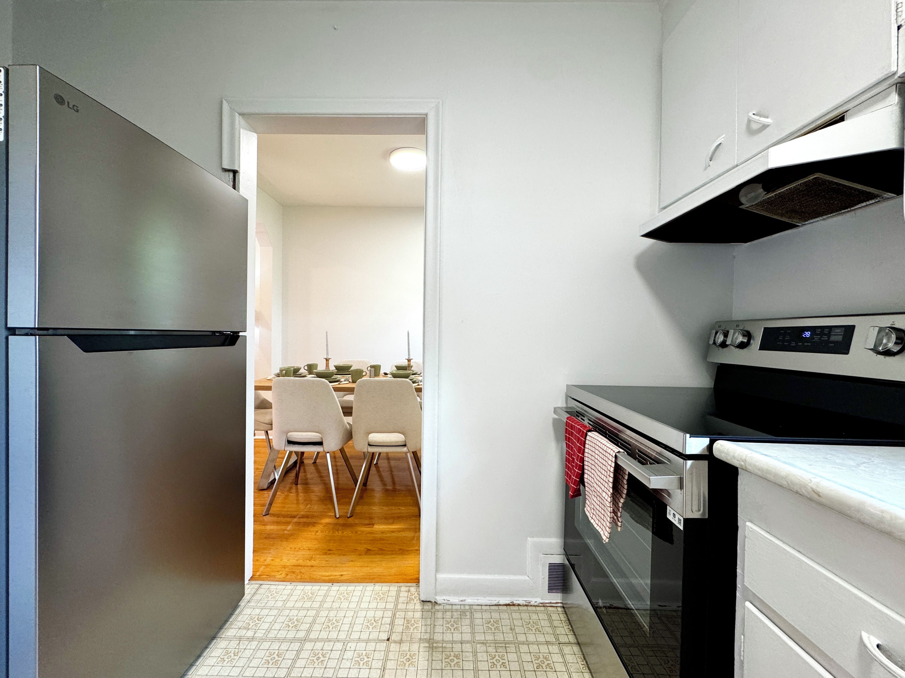 A kitchen with a refrigerator, oven, and dining area with chairs and a table.