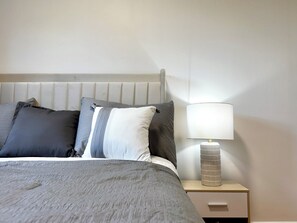 A neatly made bed with a grey bedspread and multiple pillows, a bedside lamp, and a small bedside table with a vase. - Newly Furnished Entire House (Toronto)