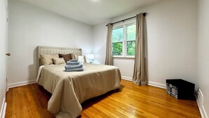 Quarto com cama, janela com cortinas, mesa de cabeceira e lixeira.