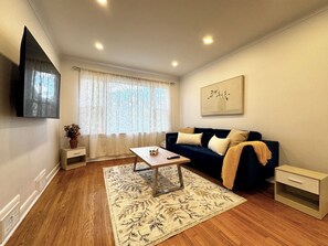 A living room with a sofa, a coffee table, a TV mounted on the wall, a window with curtains, and a painting. - Newly Furnished Entire House (Toronto)