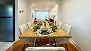 Uma sala de jantar com uma mesa de madeira posta para quatro pessoas, rodeada por cadeiras.