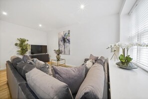 A modern living room with a grey sofa, a flat-screen TV, a painting, and a potted plant. - Eton High Street 5-Bed Townhouse | Castle Views | Parking (Eton)