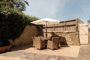 Eine Außenpatio mit Tisch und Stühlen, einem weißen Sonnenschirm und einer Steinmauer.