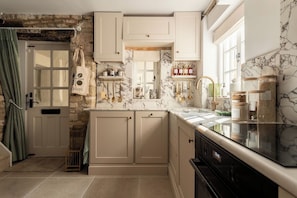 A kitchen with marble backsplash, white cabinetry, and a black stove. - Beautifully renovated cottage in Burford (Oxfordshire)