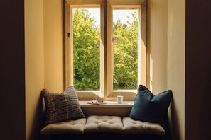 Ein Fensterplatz mit Kissen, einem Buch und einer Tasse.