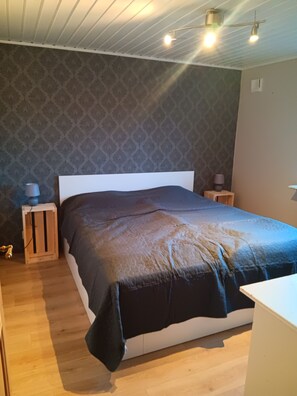 Ein Schlafzimmer mit einem Bett, Nachttischen aus Holz, einer Lampe und Wandpapier mit Muster.