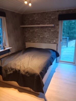 Ein Schlafzimmer mit Bett, Fenster, einer Steinsäule und einer Tür, die nach draußen führt.