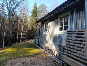 Eine Holzhütte mit einem großen Ventilator, einer Holzterrasse und einer bewaldeten Gegend.