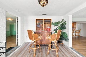 A dining area with a wooden table and two wicker chairs, a glass wall with a 'SEAFOOD' sign, and a large potted plant. - Old Florida Charm / Historic Fishing Village / Near AMI / Canalfront (Bradenton)