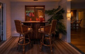A dining area with a wooden table and four wicker chairs, a neon sign reading 'SEAFOOD', and a potted plant. - Old Florida Charm / Historic Fishing Village / Near AMI / Canalfront (Bradenton)