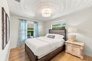 A bedroom with a large bed, a nightstand with a lamp, a window with curtains, and a ceiling with a light fixture. - Old Florida Charm / Historic Fishing Village / Near AMI / Canalfront (Bradenton)