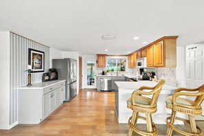 A modern kitchen with a central island, wooden cabinets, and a view to the outdoors. - Old Florida Charm / Historic Fishing Village / Near AMI / Canalfront (Bradenton)