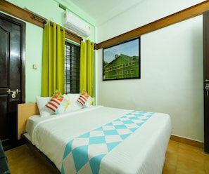 A hotel room with a bed, green curtains, a window with a view of a green building, and an air conditioning unit. - Deluxe Room Green Heaven (Kanayannur)