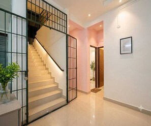 A staircase with a metal railing leading to an upper floor, a door with a doormat, and a framed picture on the wall. - Deluxe Room Green Heaven (Kanayannur)