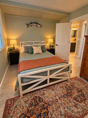 A bedroom with a bed, bedside lamps, a decorative fish wall hanging, a patterned rug, and a view into the adjacent kitchen. - Tropical Oasis in dowtown 2 blocks from the Harbor (Punta Gorda)