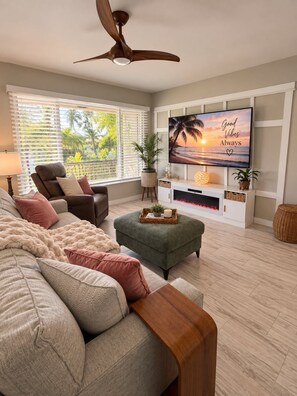 A living room with a sofa, armchair, ottoman, TV, fireplace, and a ceiling fan. - Tropical Oasis in dowtown 2 blocks from the Harbor (Punta Gorda)