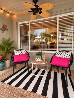 A room with two black chairs with polka dot cushions, a small round table with a candle, and a black and white striped rug.