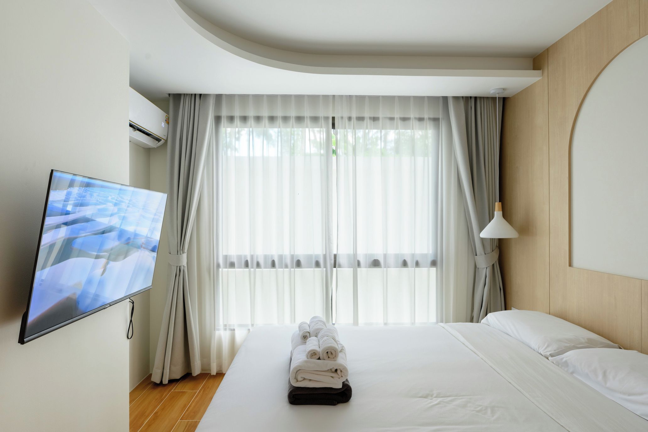 A hotel room with a bed, a TV, and a window with curtains.