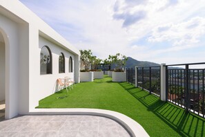A modern outdoor patio with artificial grass, a seating area, and a view of a mountainous landscape. - Kamala - Jungle View for Families (Tambon Kamala)