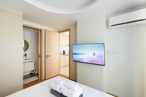A modern hotel room with a bed, a TV on the wall, a bathroom with a sink, and a door leading to the kitchen. - Kamala - Jungle View for Families (Tambon Kamala)