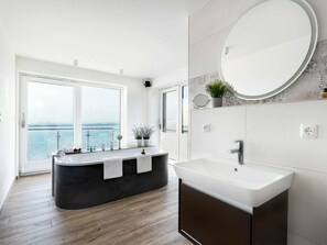 A modern bathroom with a bathtub, a sink, and a large mirror. There is a view of the sea through a large window. - Holiday Apartment With 1 Bedroom (Kappeln)