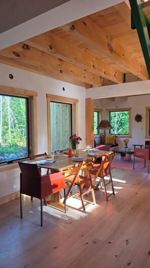 A dining area with a wooden table, chairs, and a view of the outdoors. - Beautiful Modern Cabin on 90 Acres - Private Maine Woods & Lakes (Chesterville)