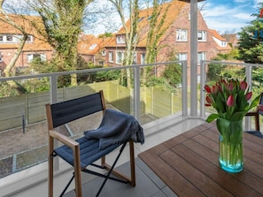 A balcony with a wooden chair, a small table, and a vase of flowers. - 248 - Apartment Anchorage (Juist)
