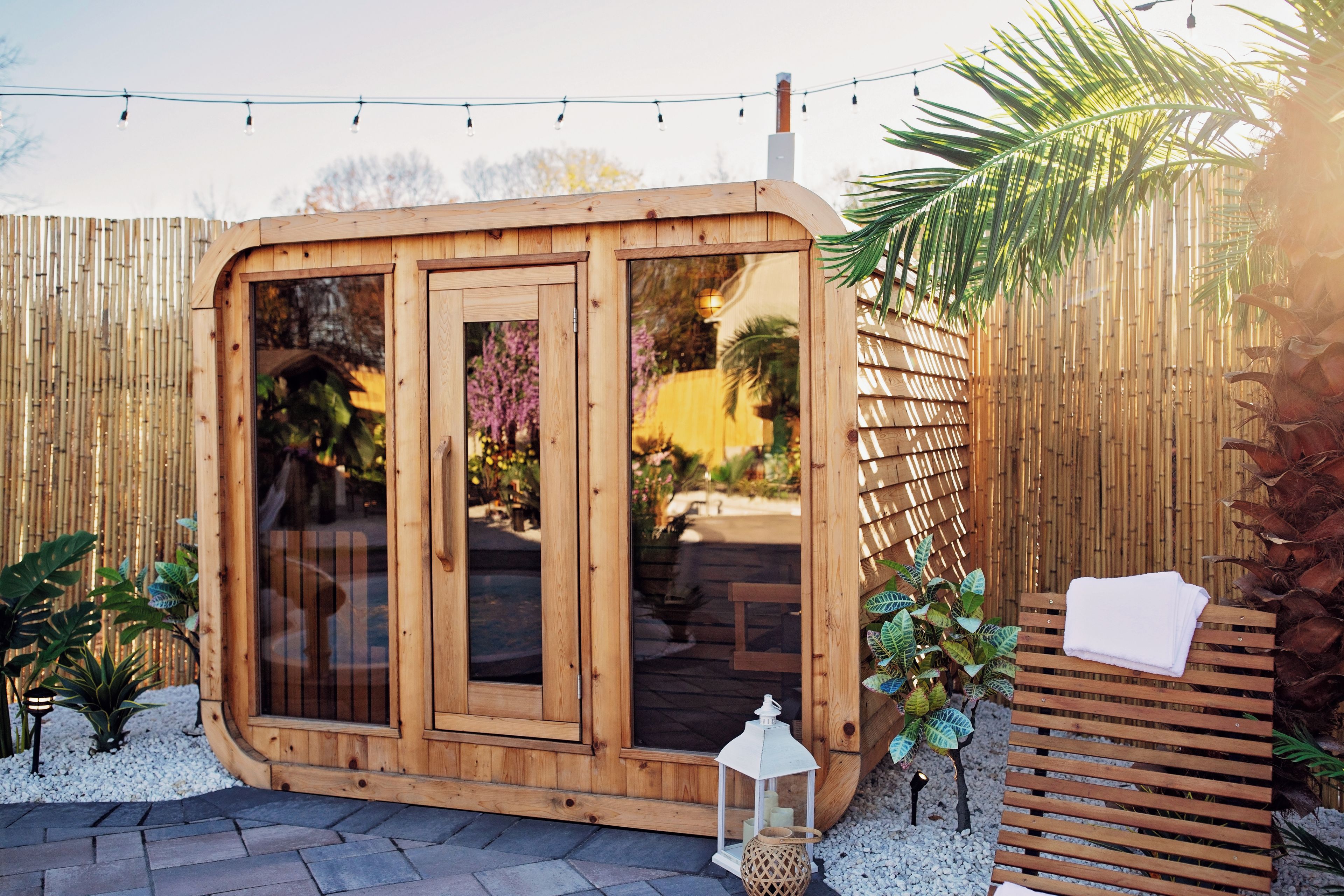 A wooden structure with glass doors, a white lantern, and a bench with a towel.