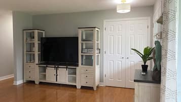 A room with a wooden floor, a white entertainment unit with a flat-screen TV, a white door, and a potted plant.