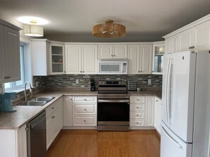 A modern kitchen with white cabinets, stainless steel appliances, and a wooden floor.