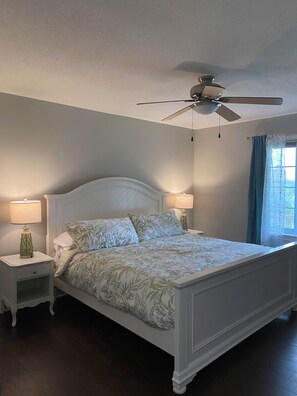 A bedroom with a bed, two bedside tables, a ceiling fan, and a window with curtains.