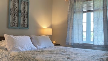 A bedroom with a bed, a ceiling fan, a window with curtains, and a wall-mounted decorative piece.