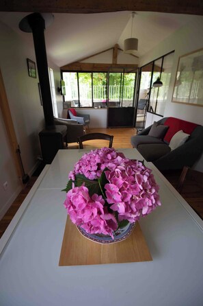 A living room with a white table, a sofa, and a large window with a view of greenery. - Le Gué Renard: A Balcony Overlooking the Charente. Pets allowed. (Jarnac)