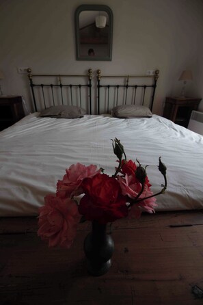 A bed with a white sheet, a vase with flowers in the foreground, and a bedside table with a lamp. - Le Gué Renard: A Balcony Overlooking the Charente. Pets allowed. (Jarnac)