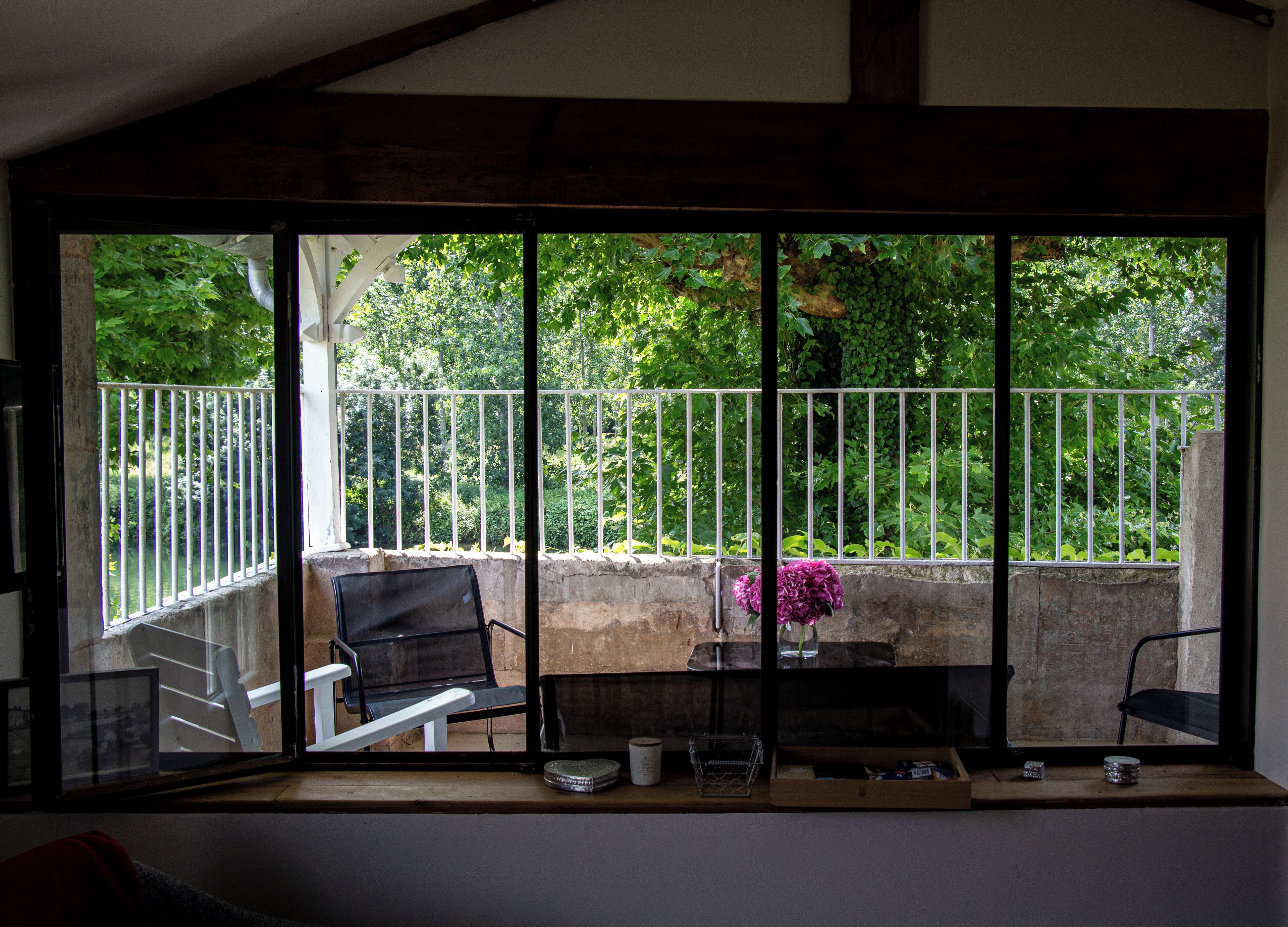 A balcony with a view of a garden, a metal railing, and a table with chairs.