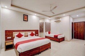 Een hotelkamer met een groot bed, een kleiner bed, een nachtkastje, een plafondventilator en een airconditioner.